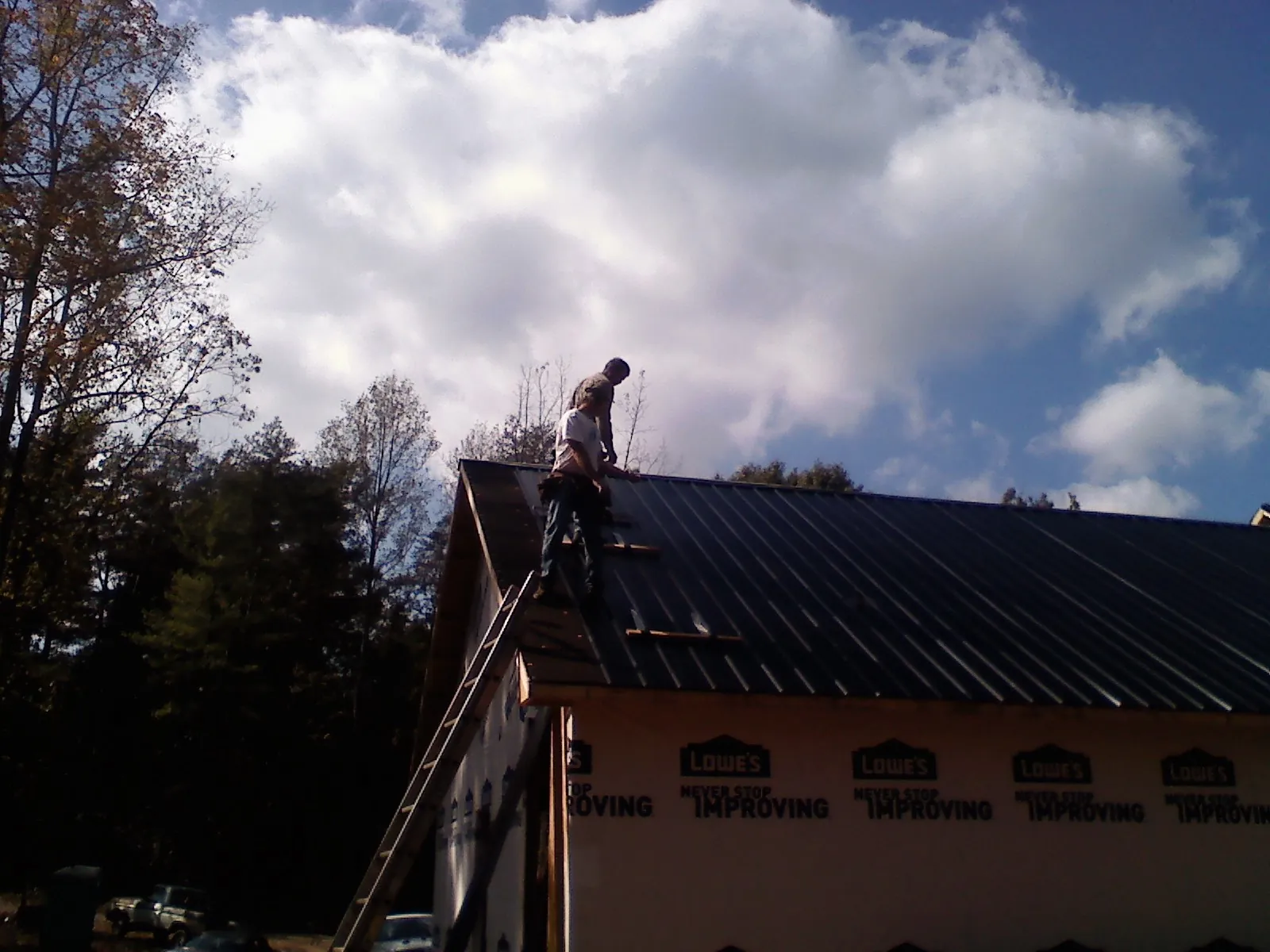 Roofer fastening dark metal panels high against a cloudy sky, from a Roof Inspection job in Cataldo
